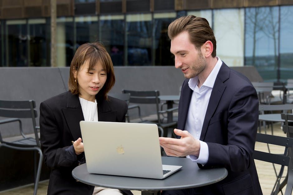 A man and a woman are sitting at a table looking at a laptop.