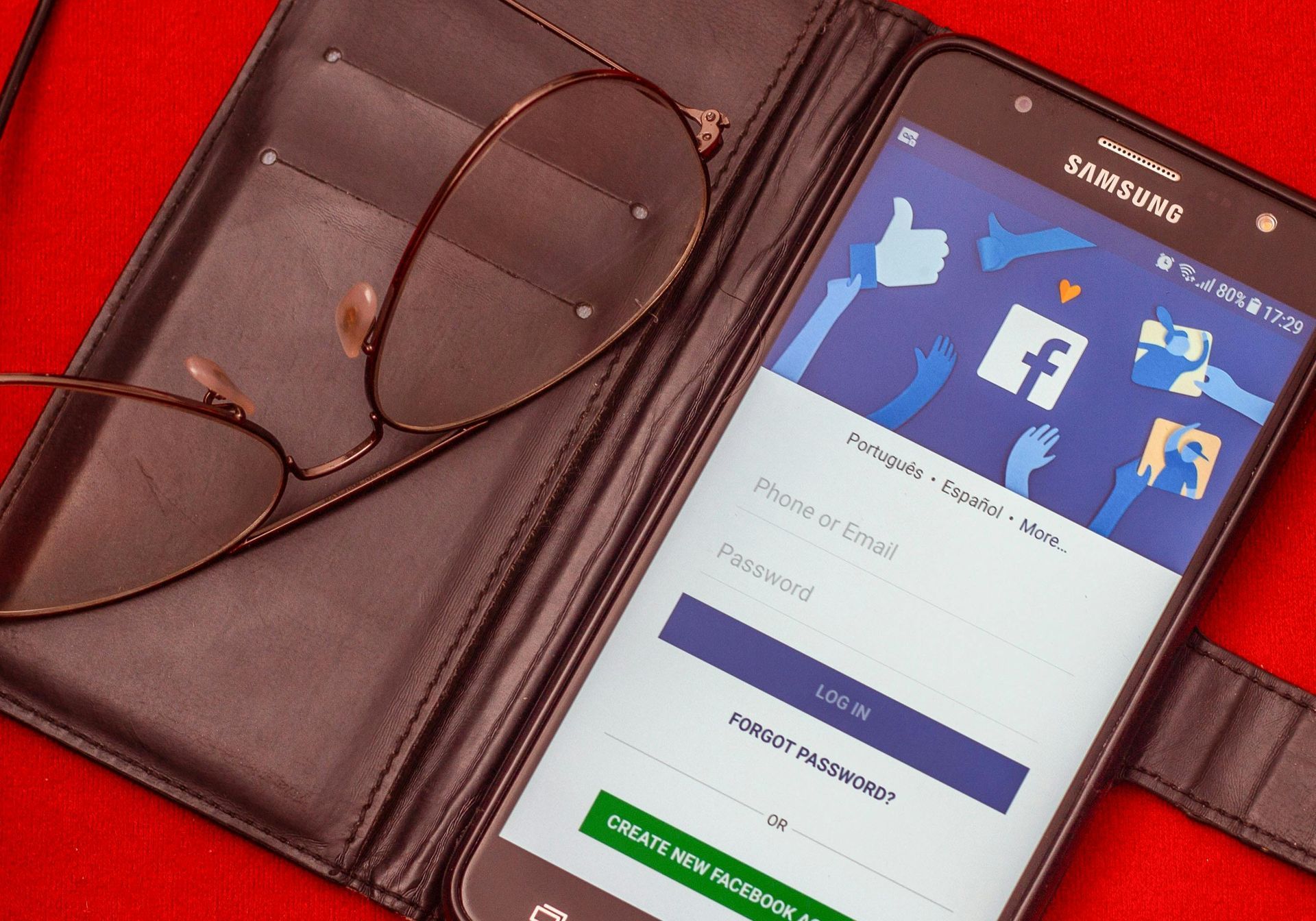 A cell phone is open to a facebook page next to a pair of glasses.