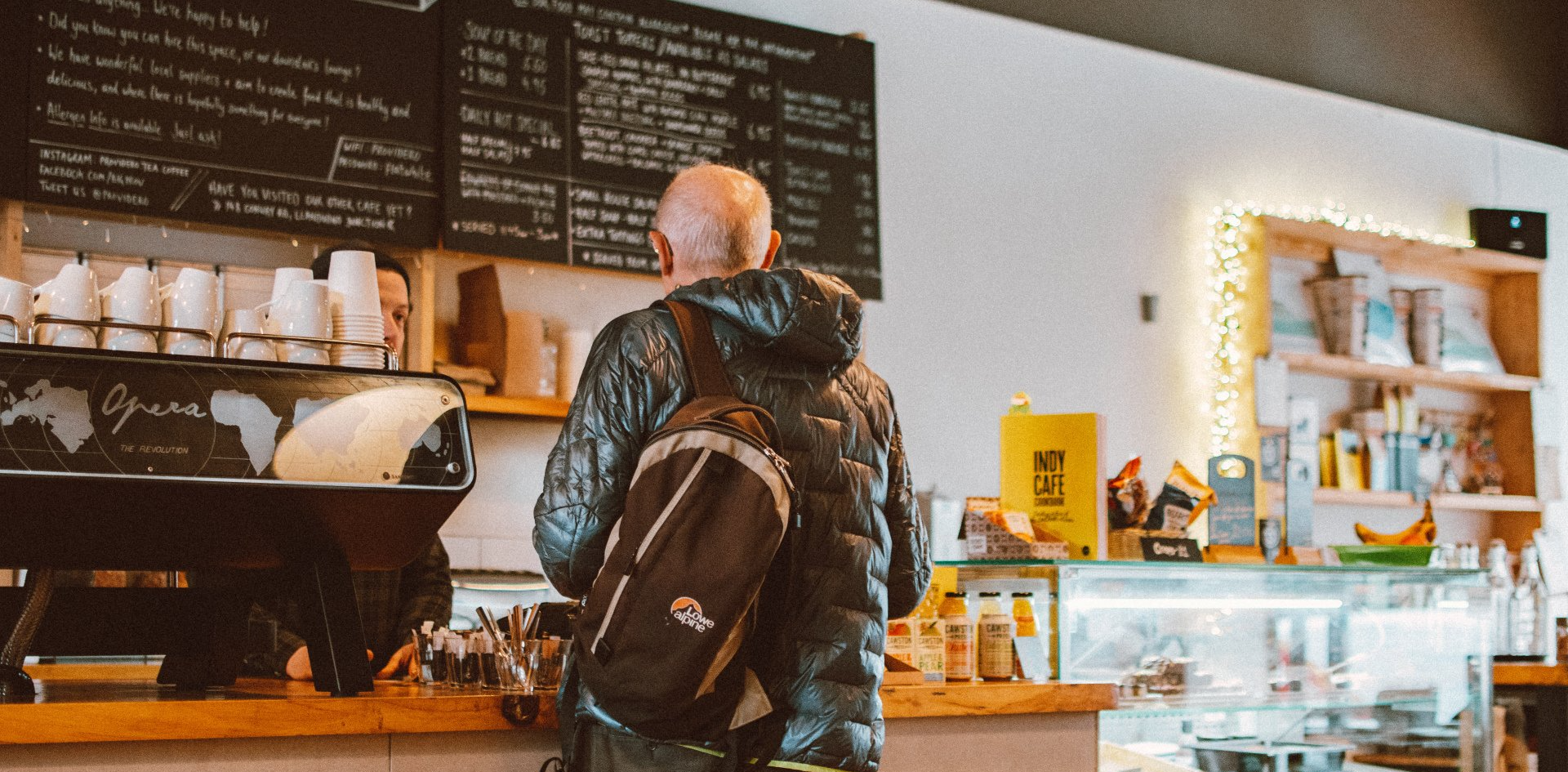 A man with a backpack is standing in a coffee shop.