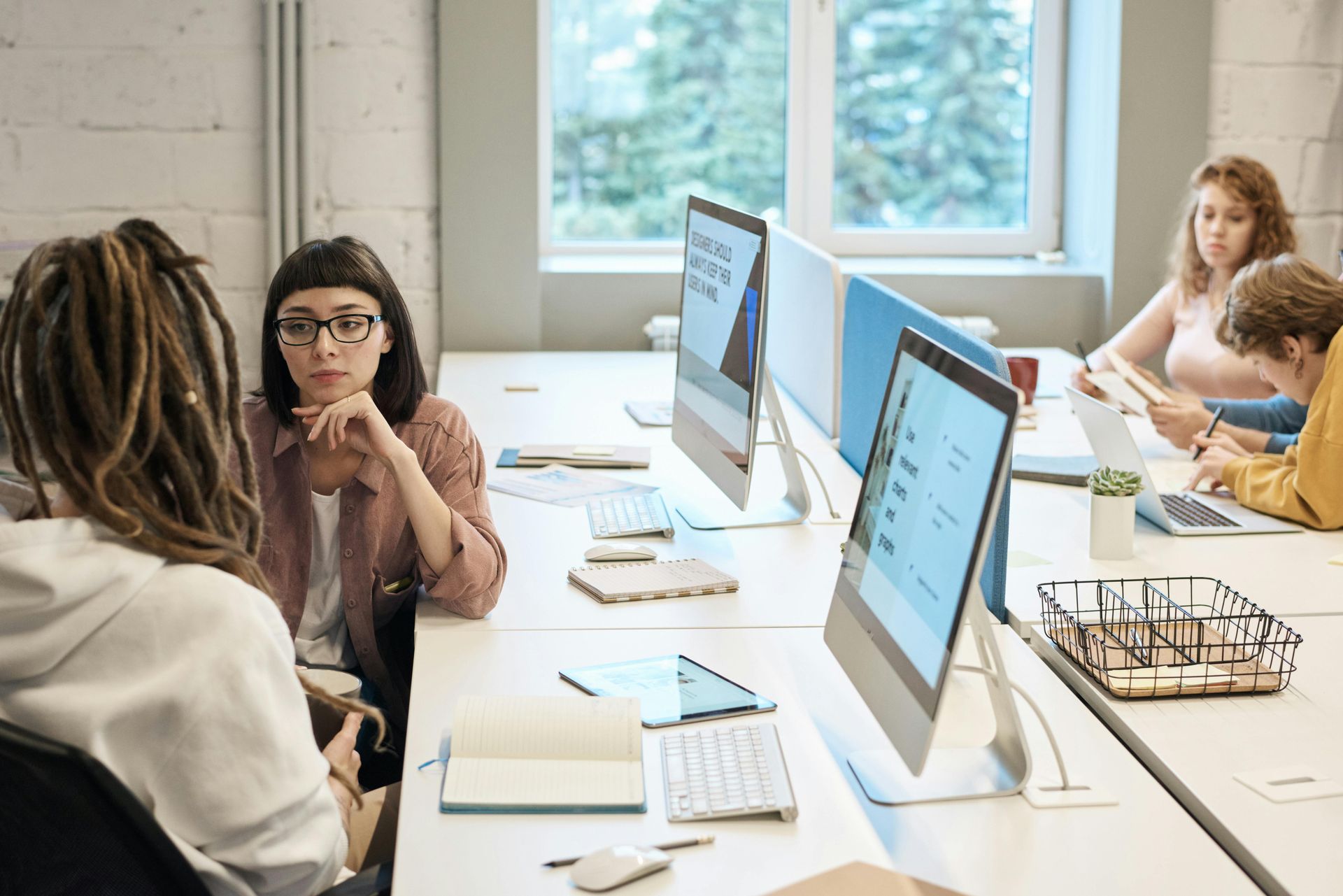 A group of people are sitting at desks in an office with computers.