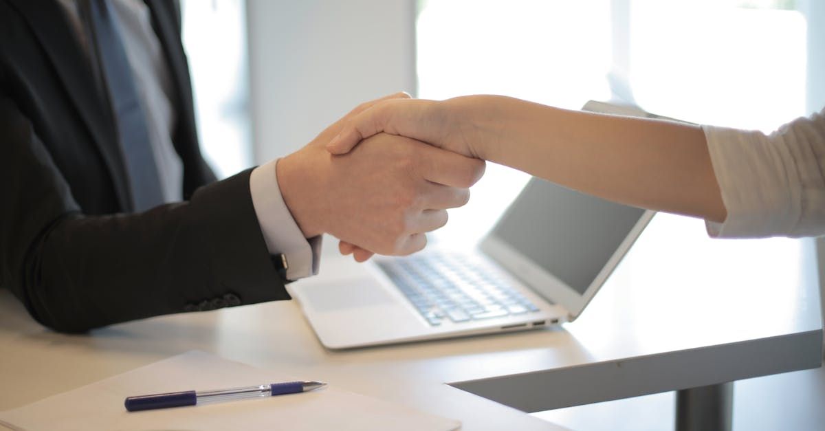 A man and a woman are shaking hands in front of a laptop.