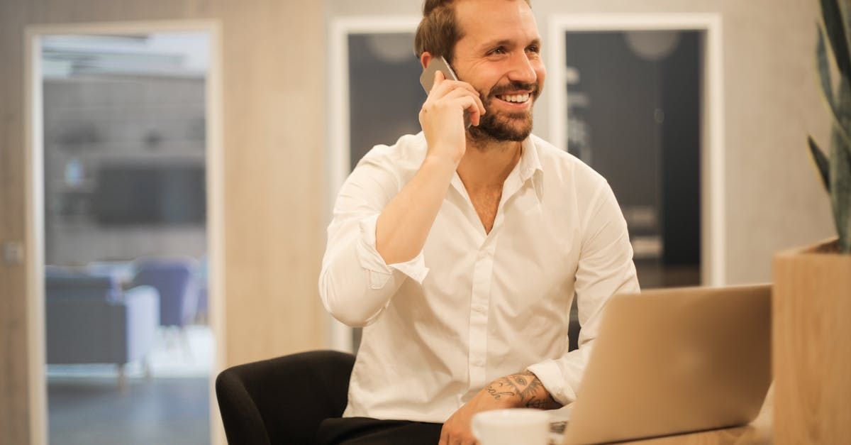 A man is sitting in front of a laptop computer talking on a cell phone.