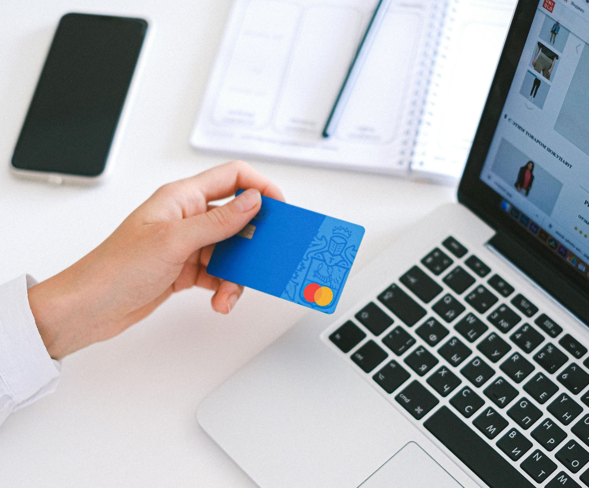 A person is holding a credit card in front of a laptop