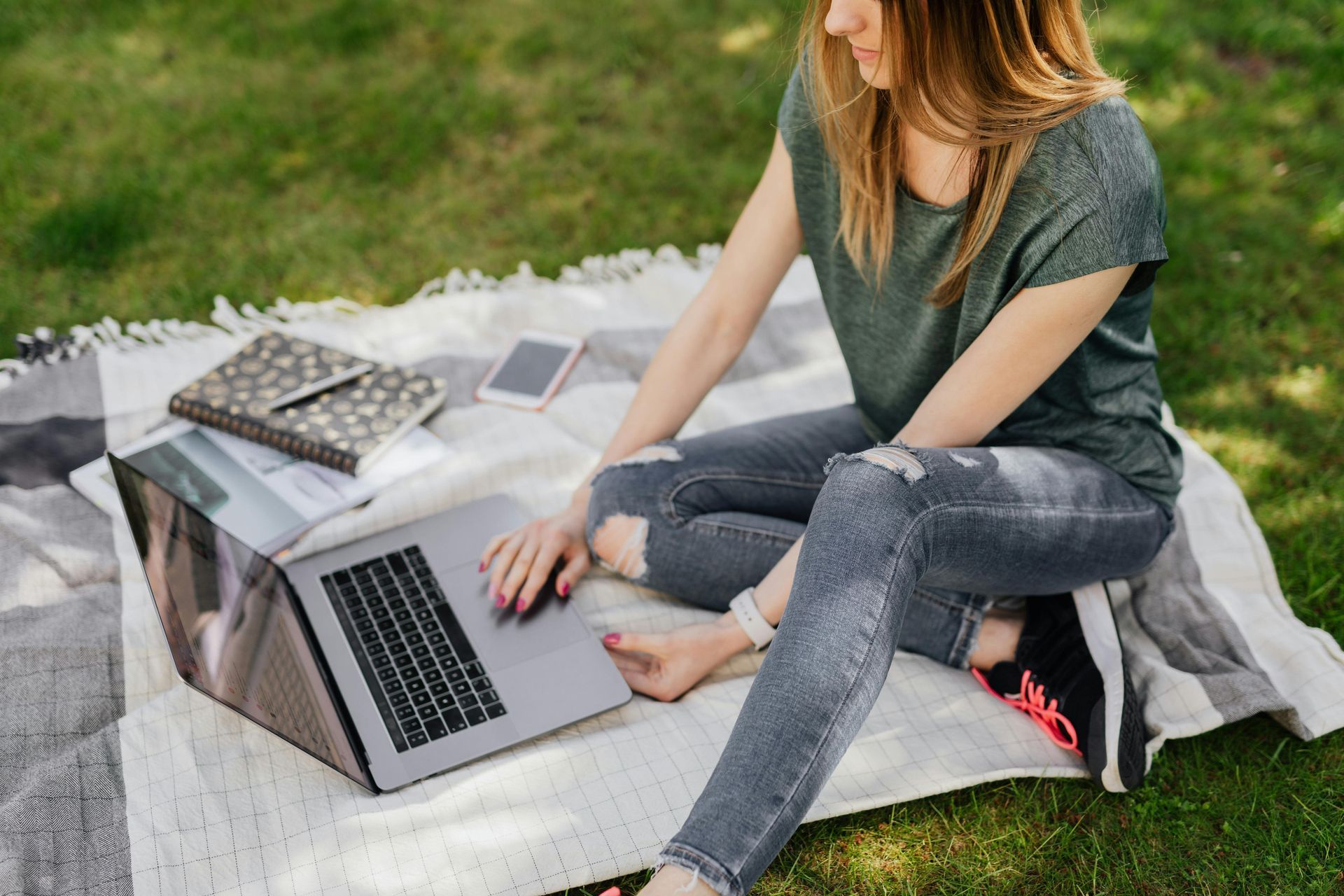 A woman is sitting on a blanket using a laptop computer.