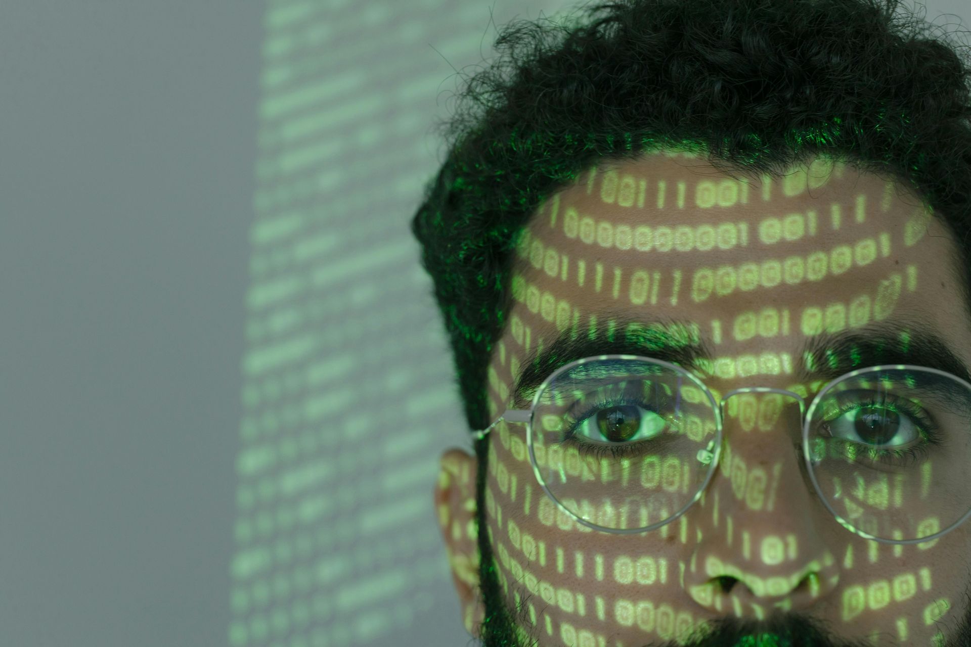 A man with glasses and a beard has binary code projected on his face.