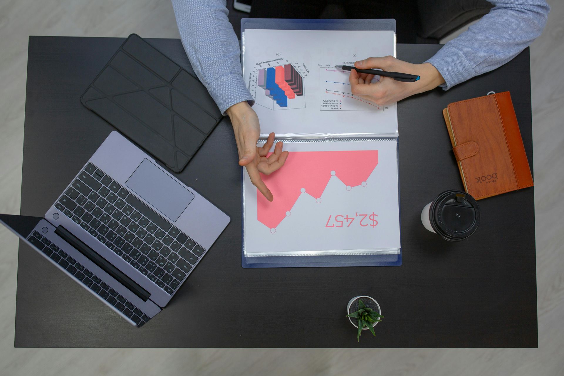 A person is sitting at a desk with a laptop and a binder.