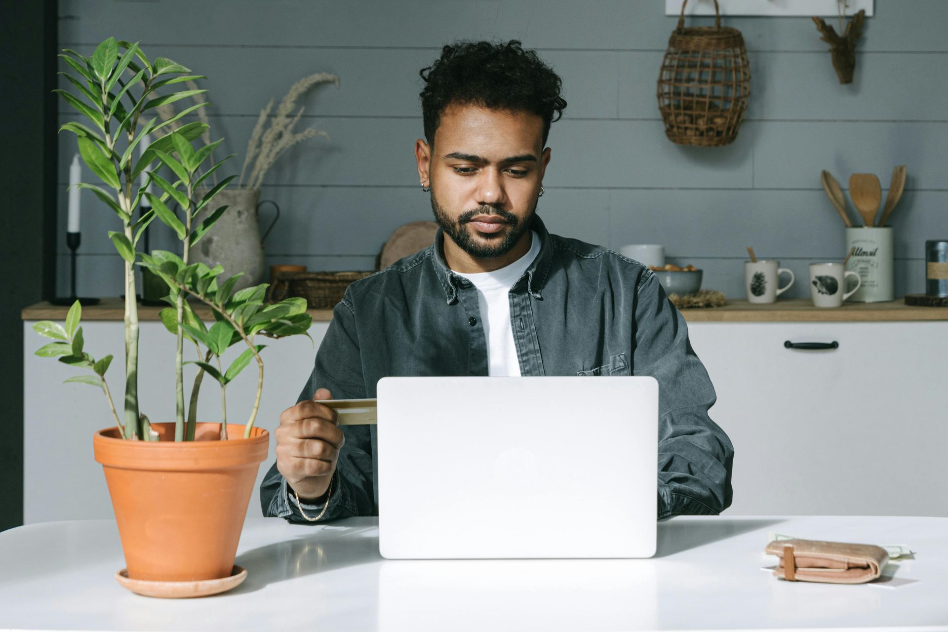 A man is sitting at a table using a laptop computer while holding a credit card.