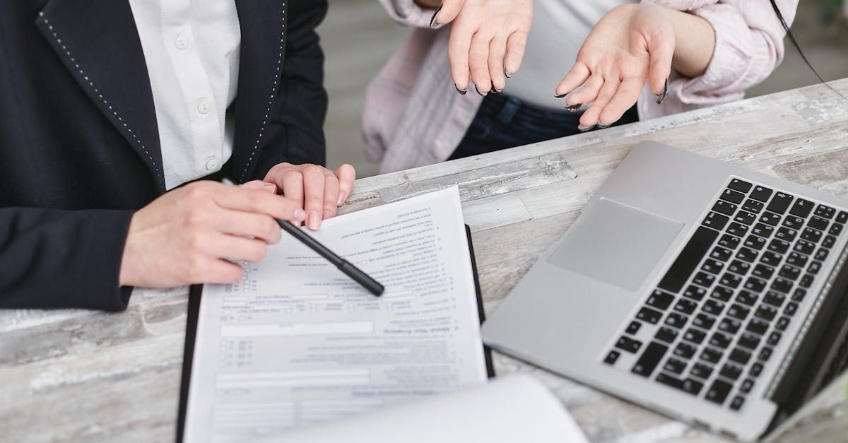 A woman is signing a document next to a laptop computer.