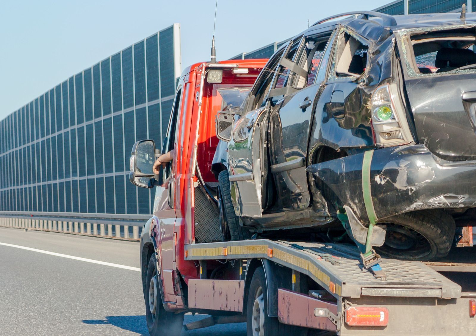A tow truck is carrying a damaged car on a highway.