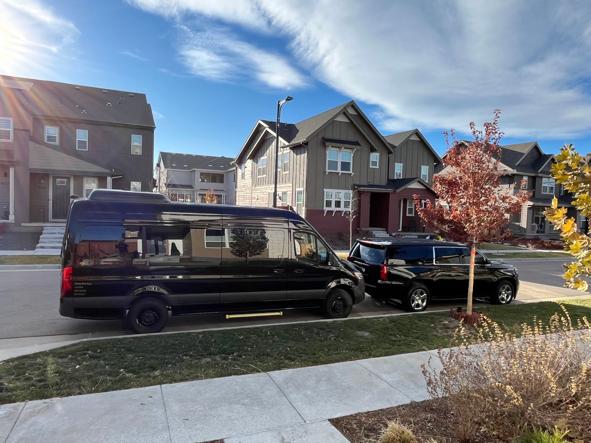 A black Ford F-series shuttle bus parked on a paved surface against a blue sky with trees in the background.