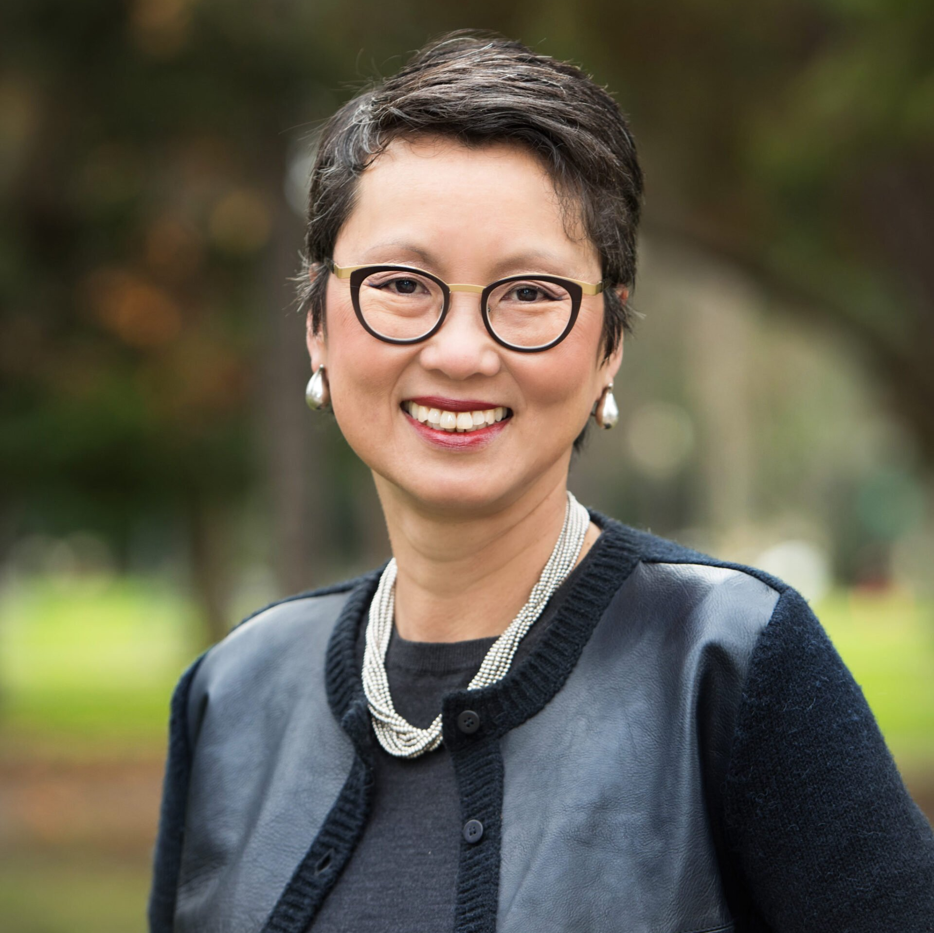 A woman wearing glasses and a pearl necklace is smiling for the camera.