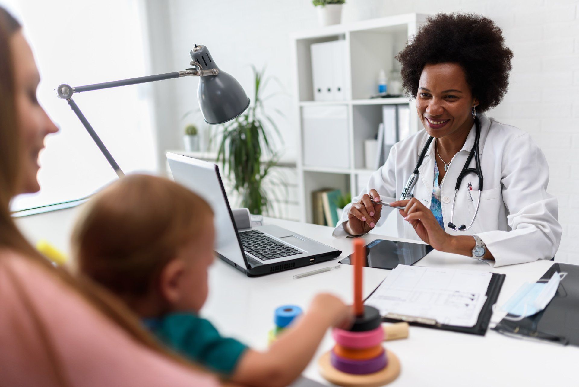 A doctor is sitting at a desk with a baby and a woman.