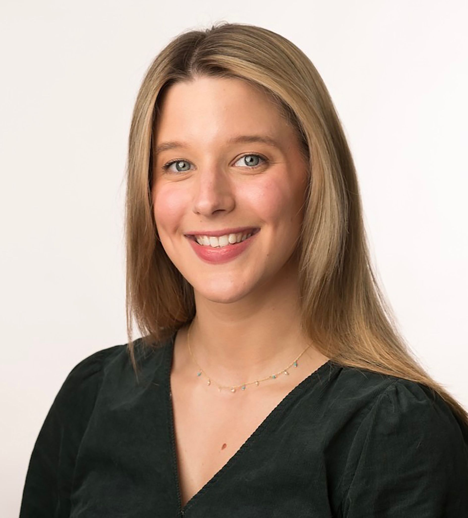 Blonde woman smiling, wearing a dark green top, against a white background.