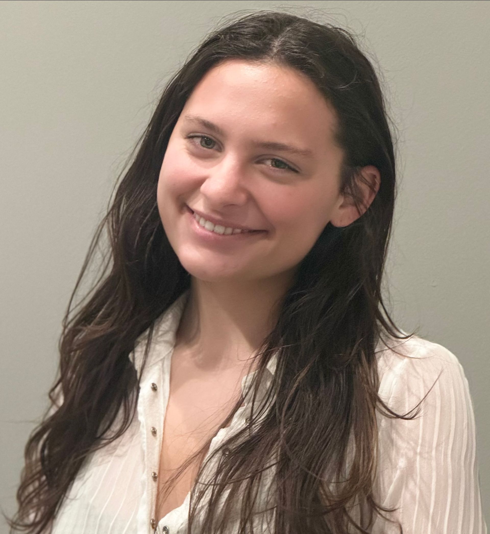 Woman smiling, wearing a white button-down shirt, with long brown hair.