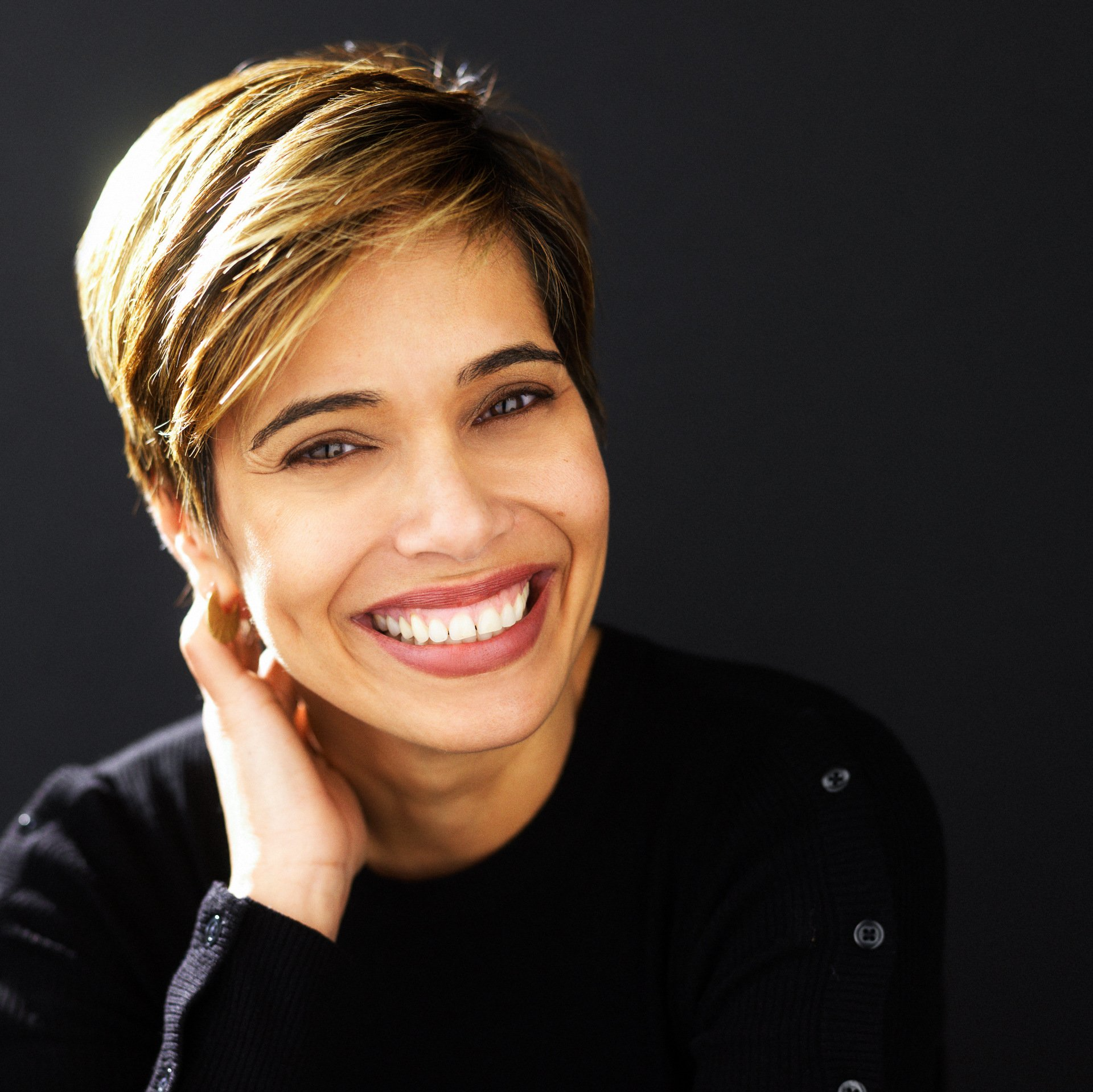 A woman with short hair is smiling with her hand on her neck