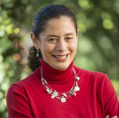 A woman wearing a red turtleneck and a necklace smiles for the camera.