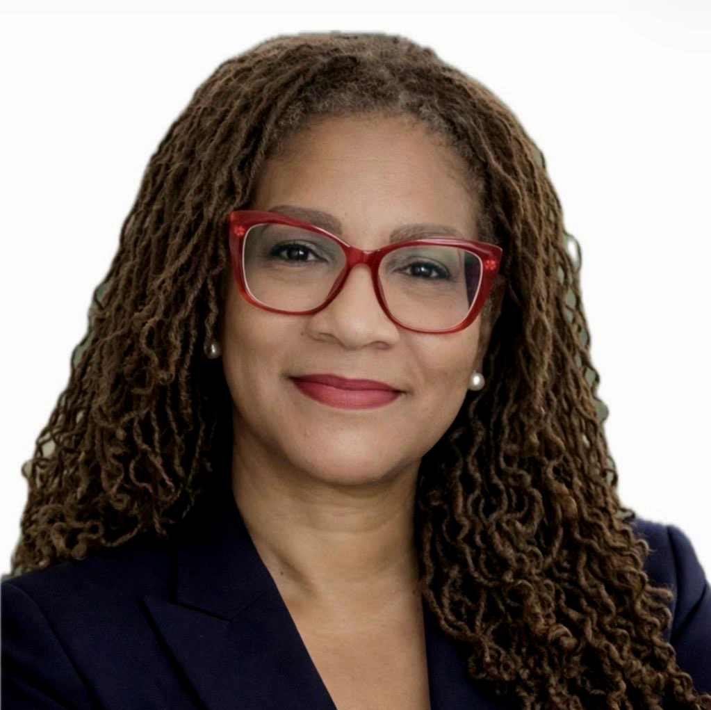 Woman with locs, smiling, wearing red glasses, against a white background.