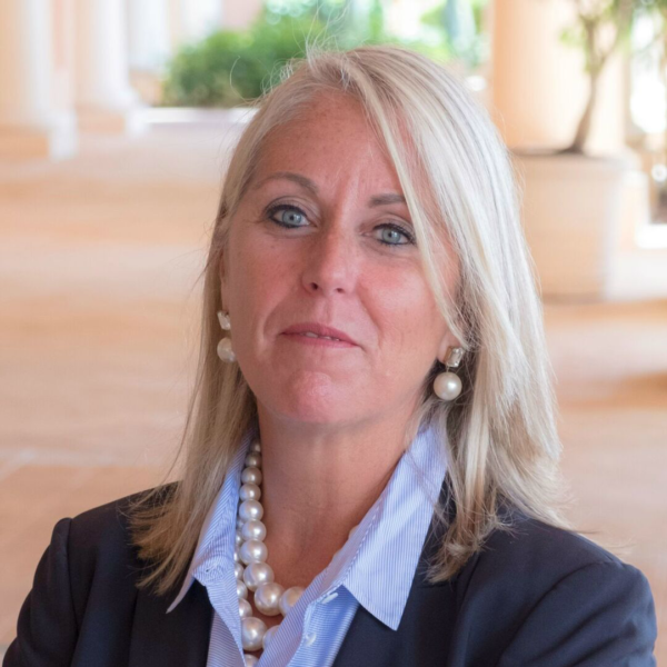Woman with blonde hair wearing a suit jacket, pearl necklace, and earrings.