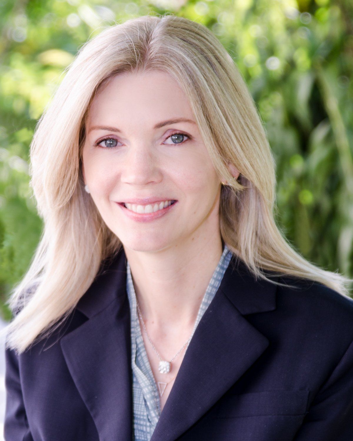 A woman wearing a black jacket and a necklace is smiling for the camera.