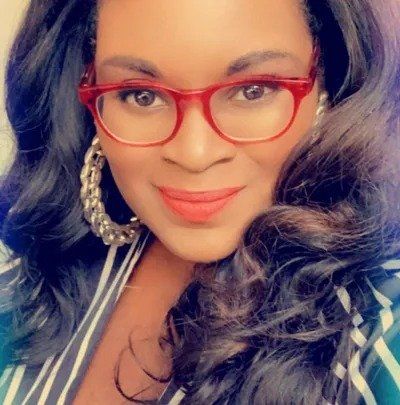 A woman wearing glasses and earrings is smiling for the camera.