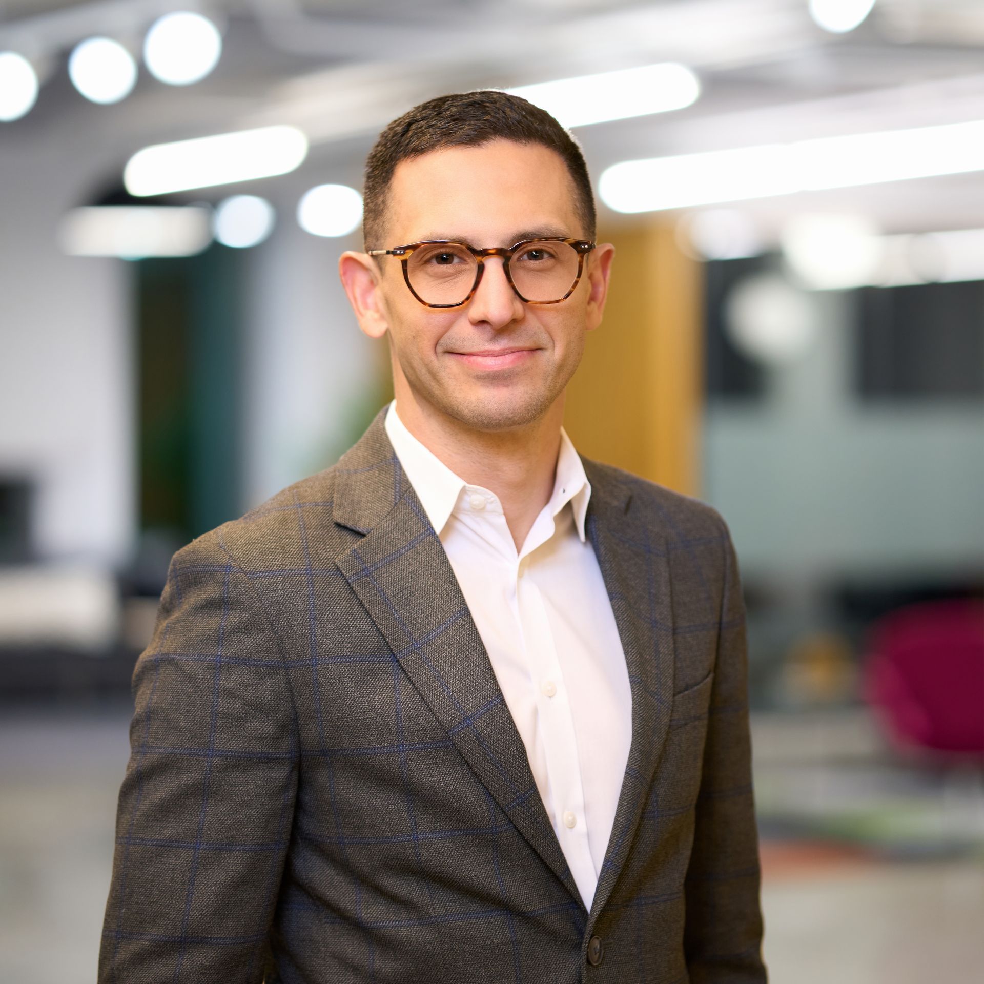 Man in glasses, grey suit, smiling against an office background.