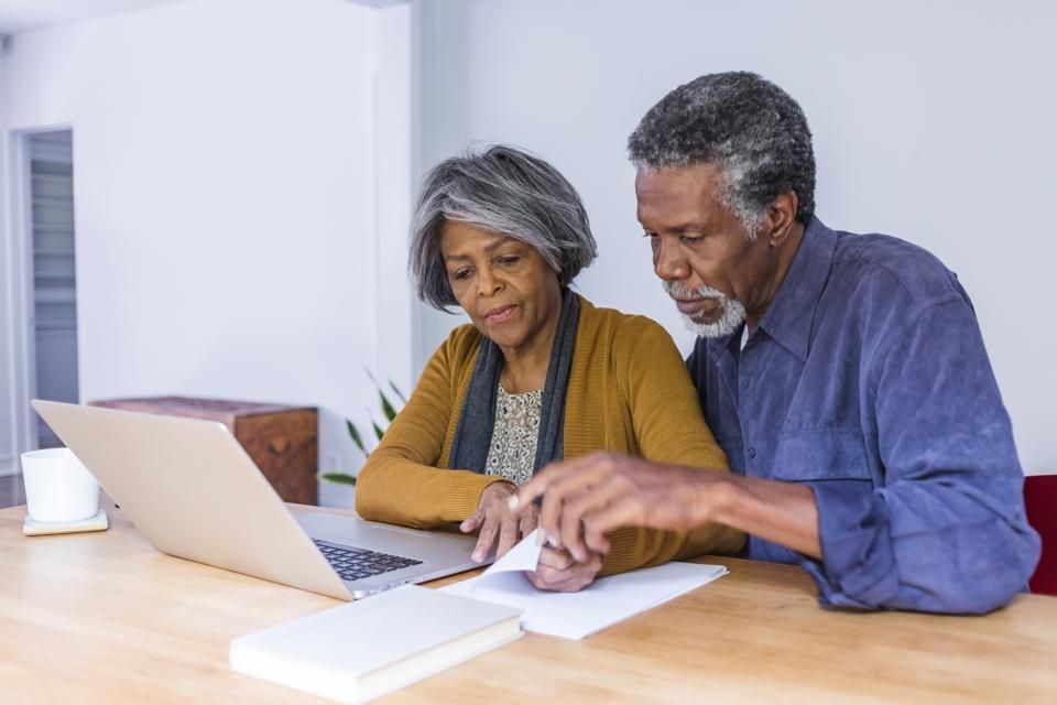 Couple looks at laptop, examining documents, sitting at table.