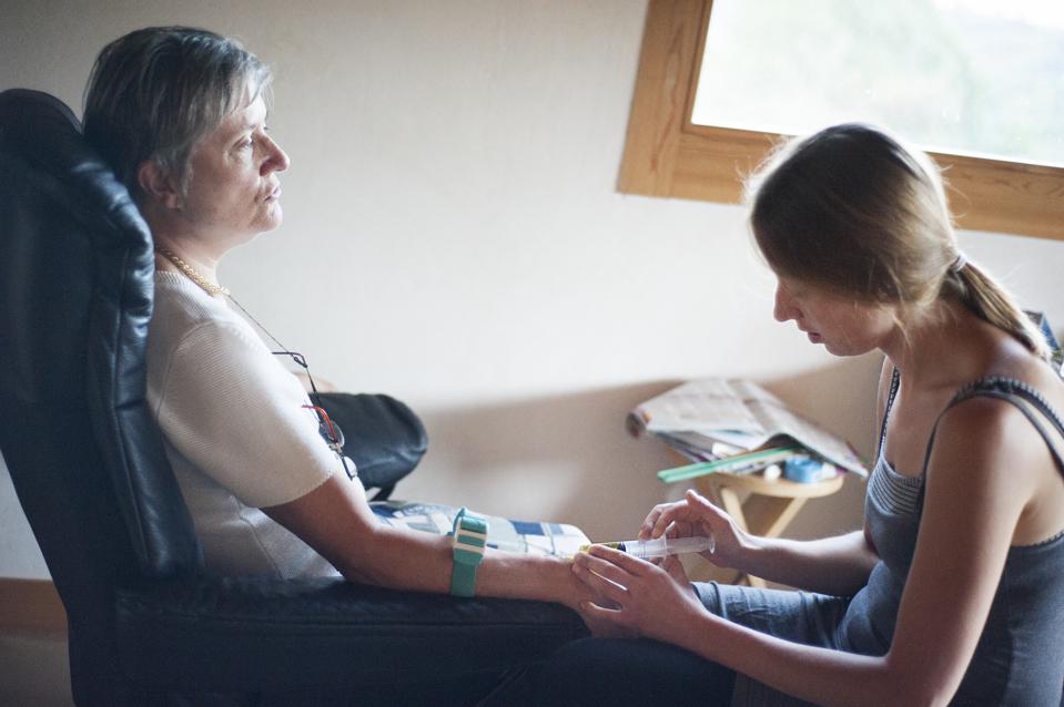 Woman receives care, another person cares for her arm in a room with light, soft colors.