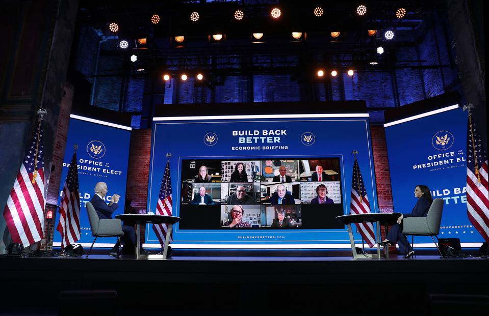 Biden and Harris seated for meeting, with video call participants on screen; American flags present.