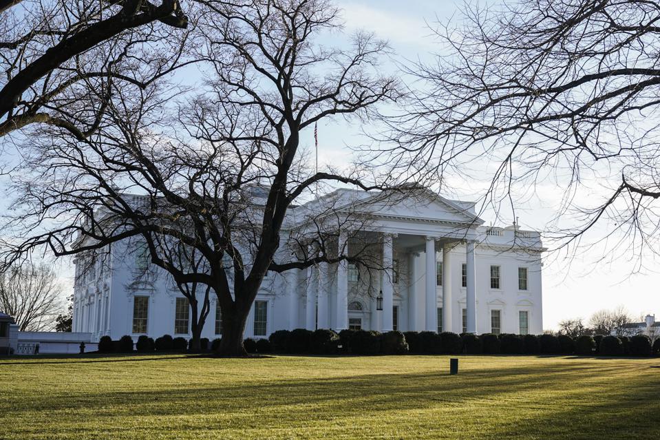 White House viewed through bare tree branches on a sunny day.