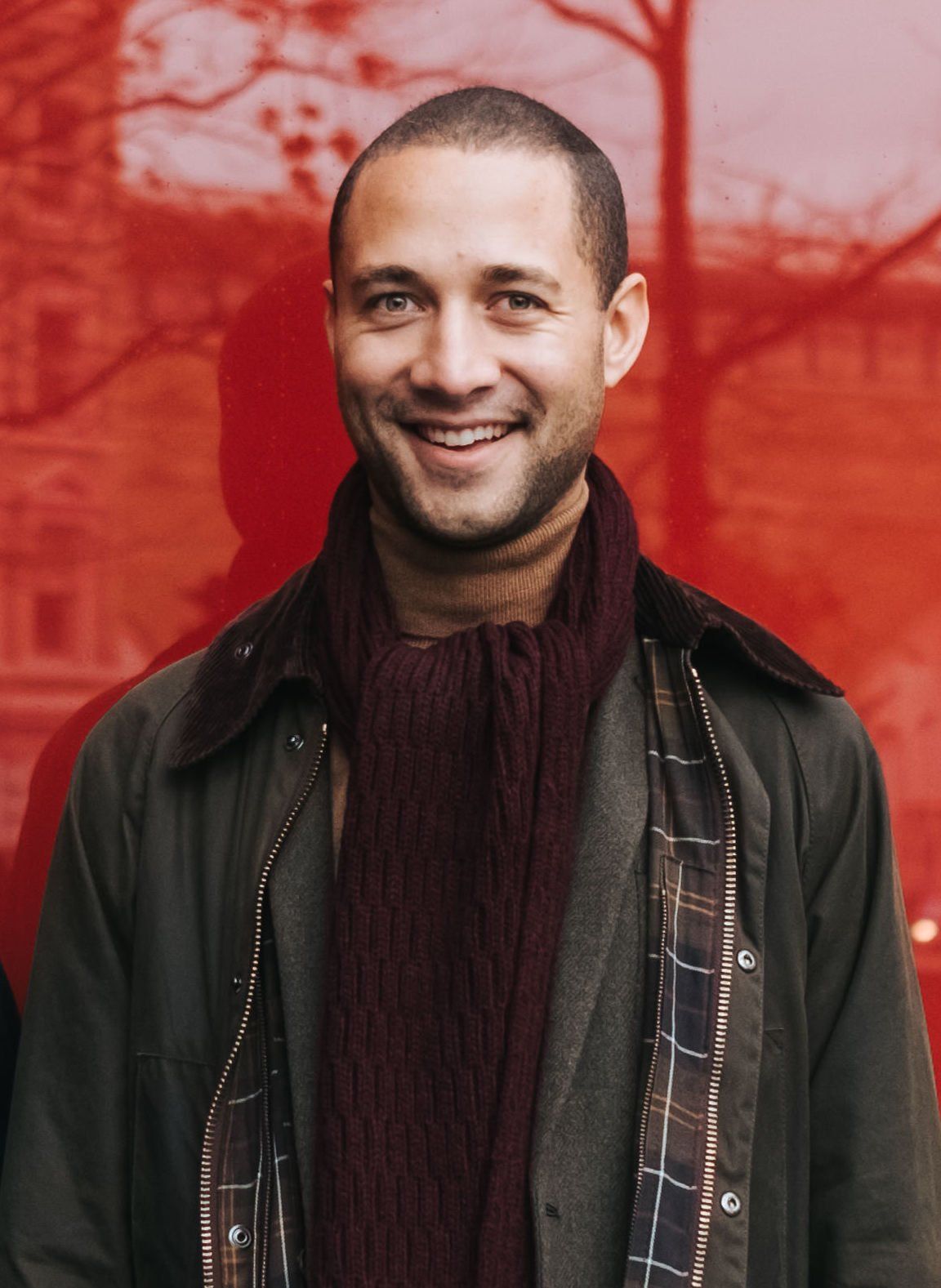 A man wearing a scarf and a jacket smiles for the camera