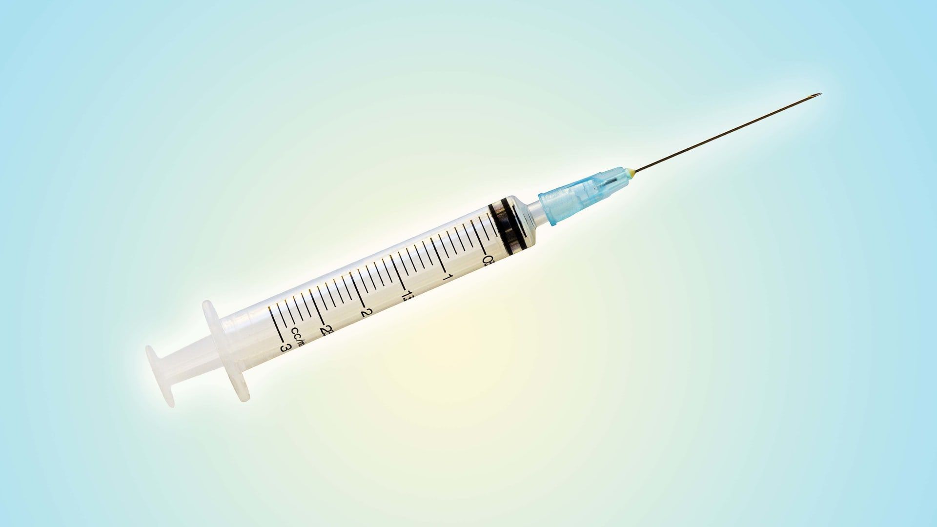 Syringe with needle, clear barrel with black markings, blue background.
