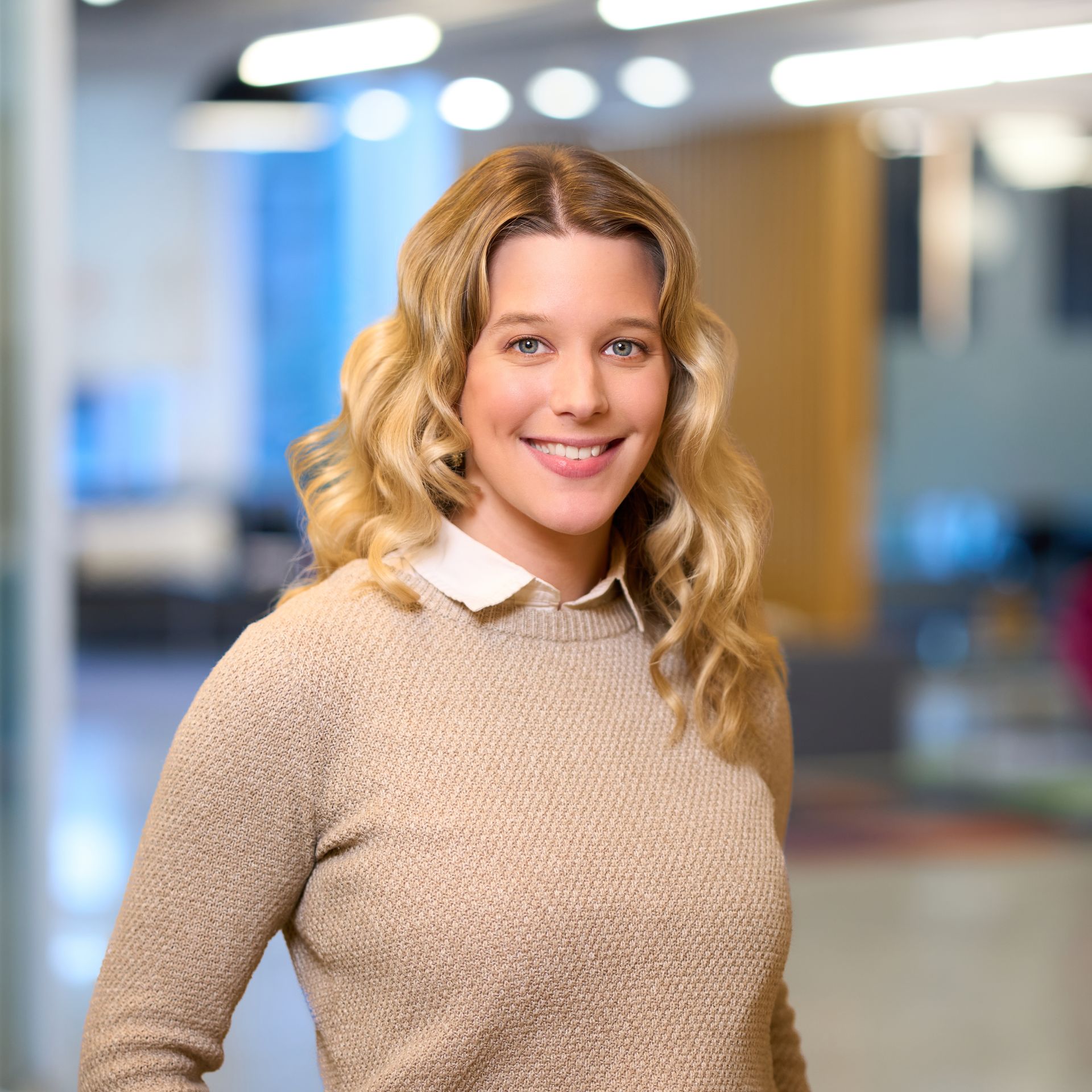 Blonde woman smiling, wearing a dark green top, against a white background.