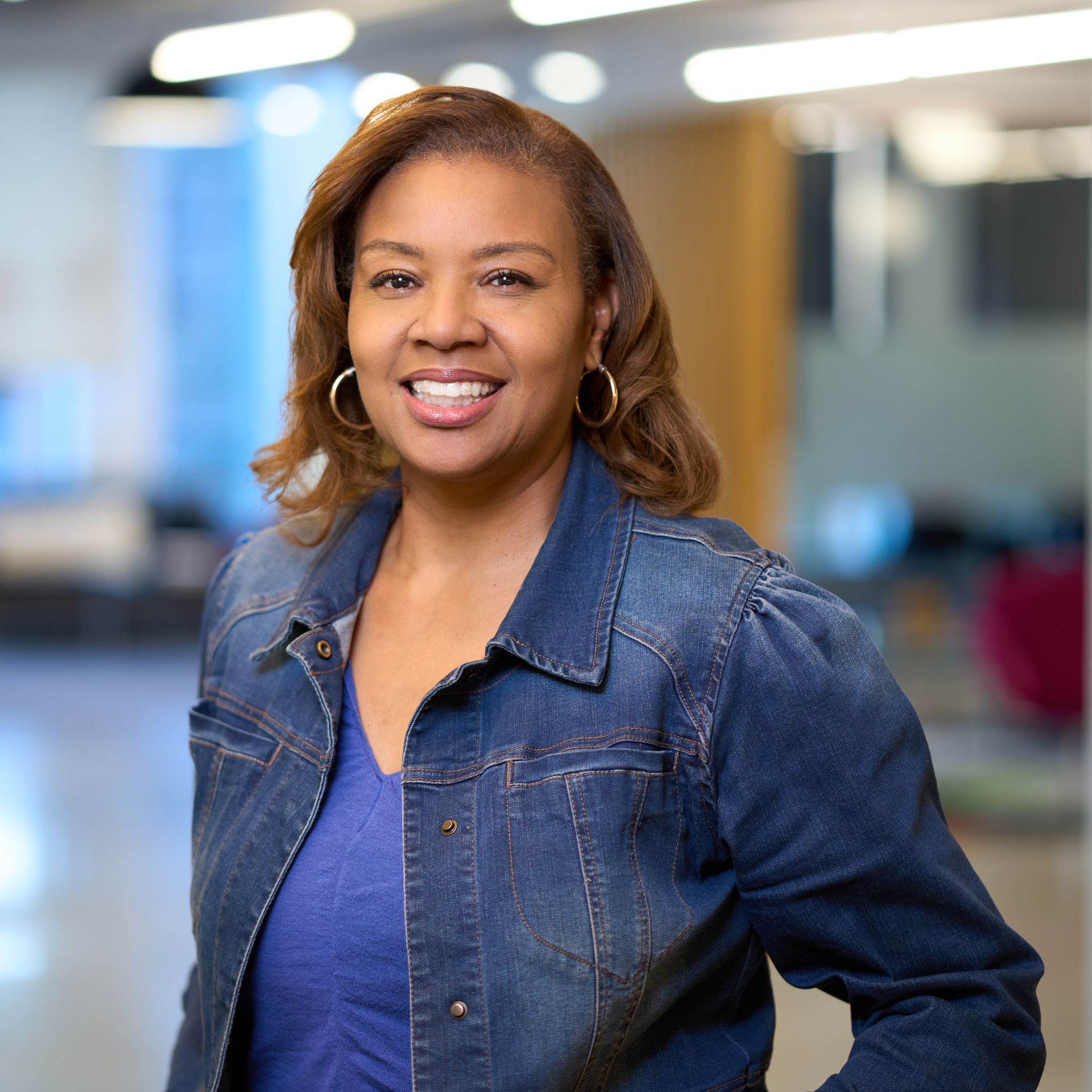 Woman in a black blazer and pink top smiles at the camera against a blue backdrop.