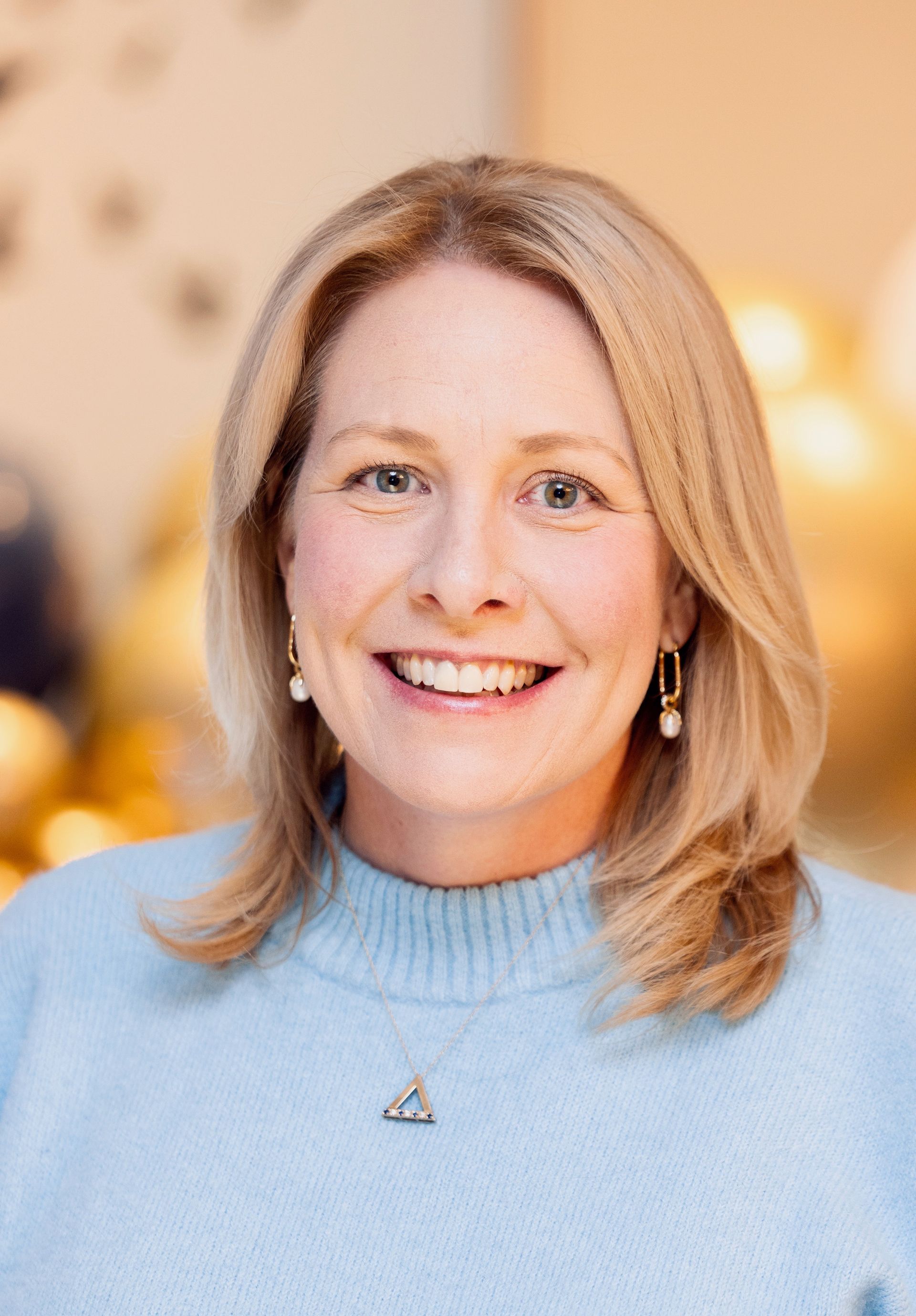 A woman wearing a black shirt and a necklace is smiling for the camera.