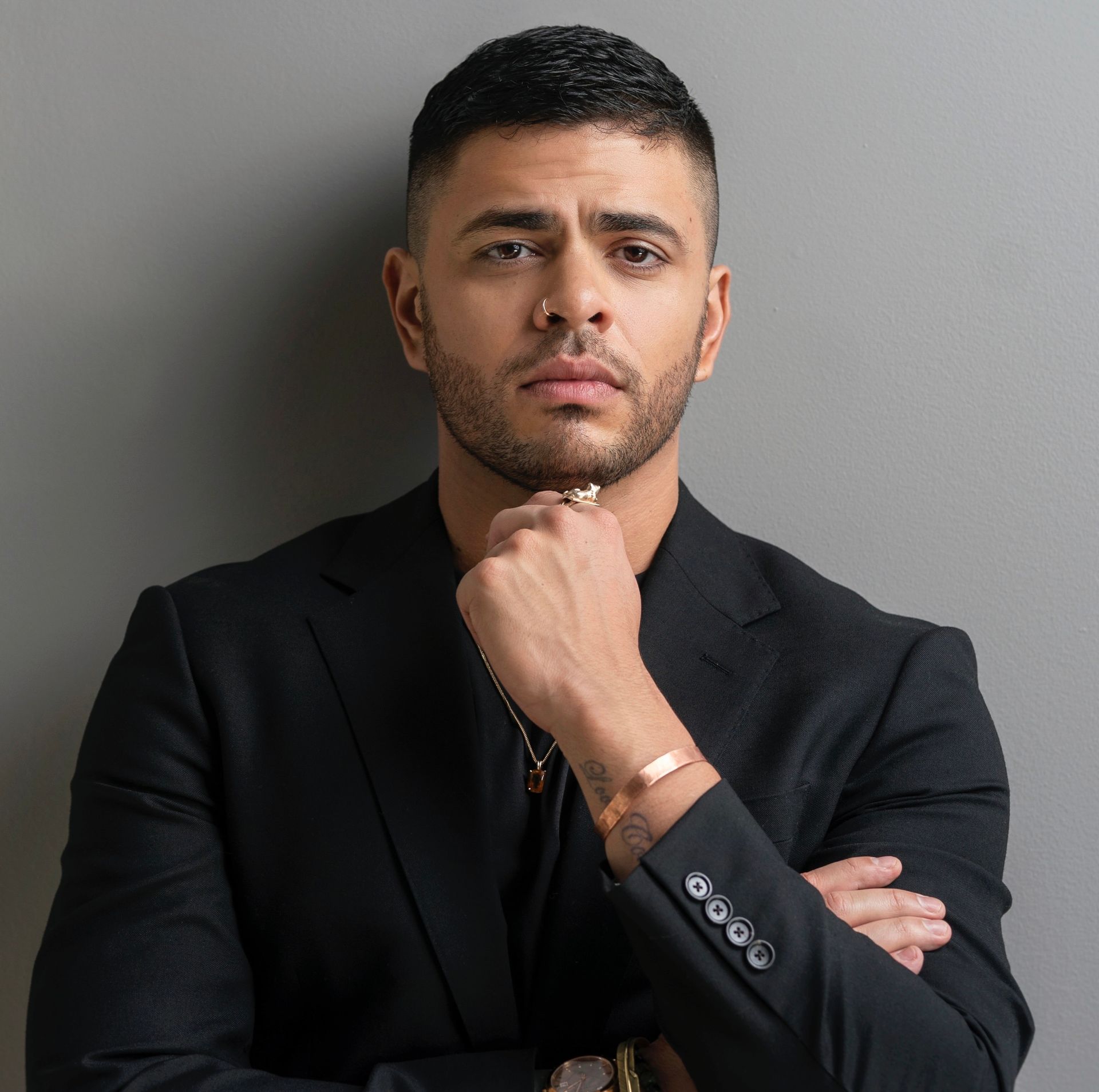 Man in black suit, hand on chin, looking at the viewer.