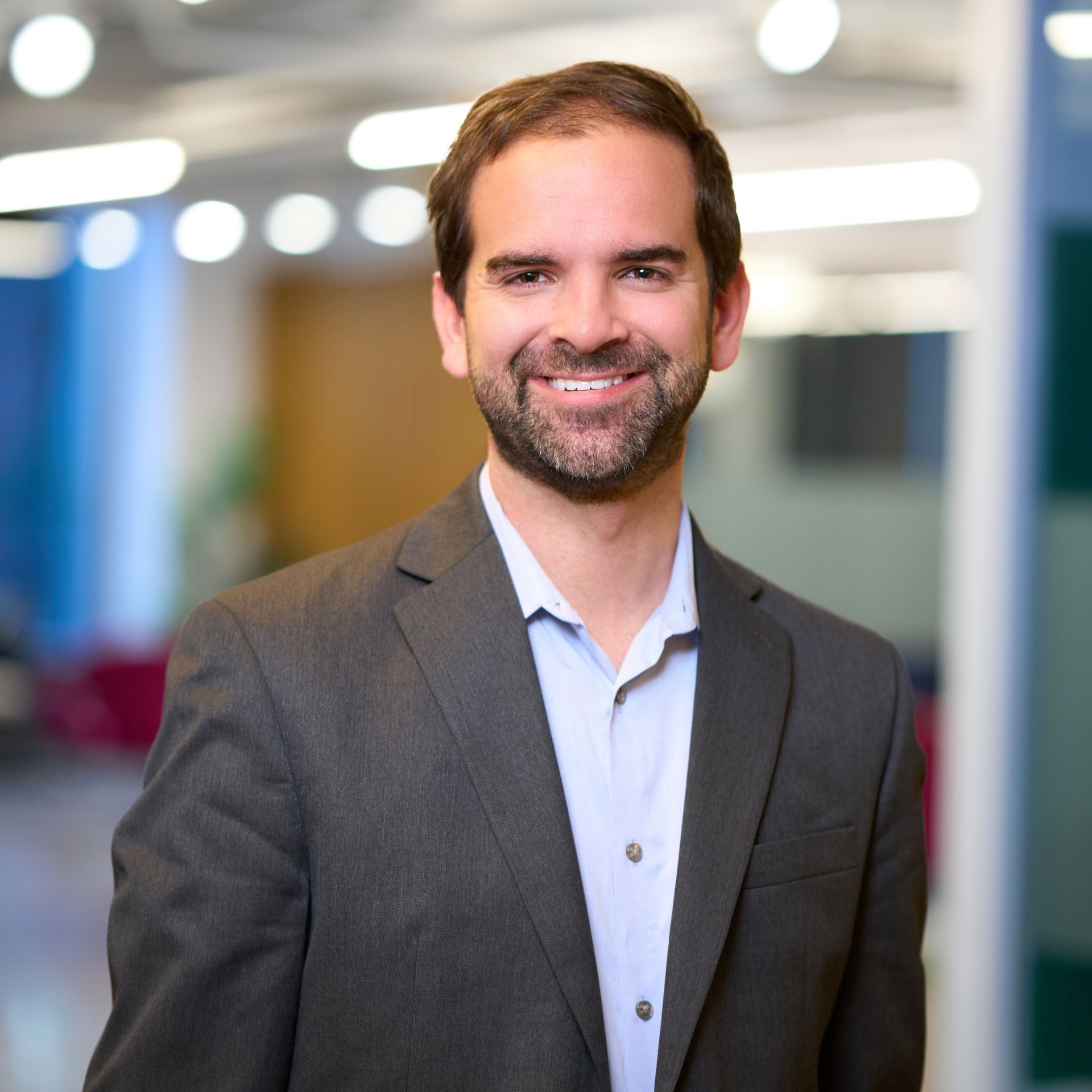 Man in a blue shirt and suit jacket smiles, against a neutral background.