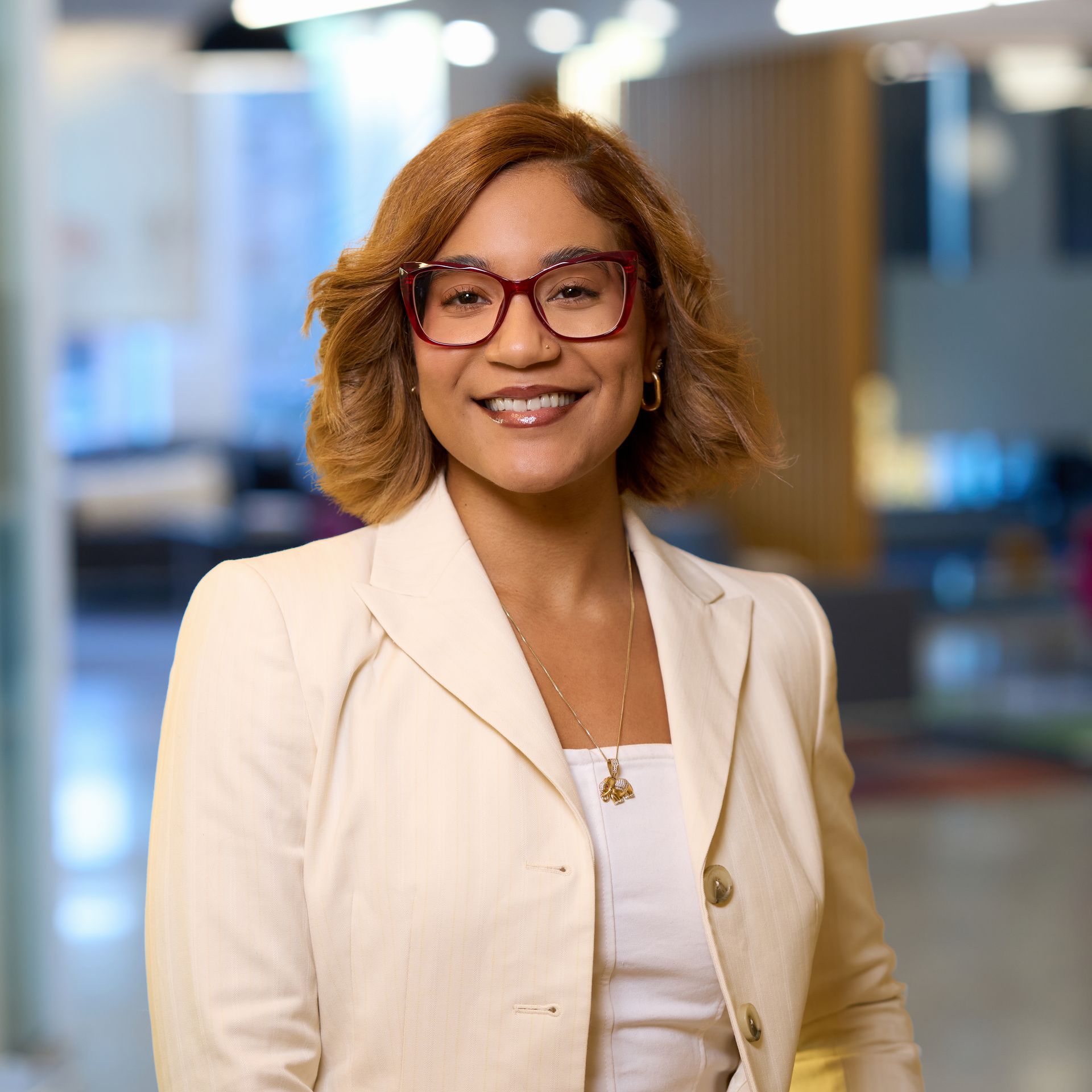 Woman with brown curly hair, glasses, and white cardigan, smiling.