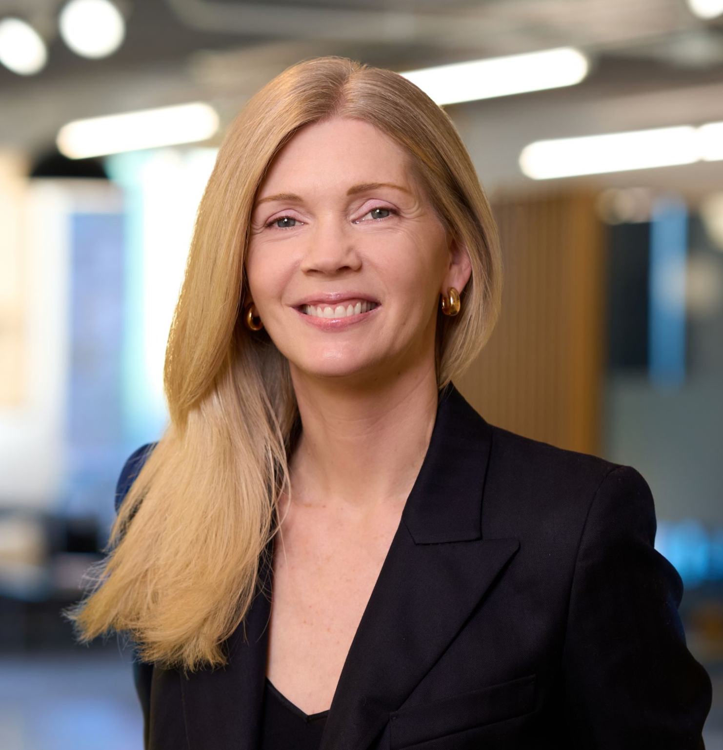Woman with blonde hair smiling, wearing a black blazer against a blurred office background.
