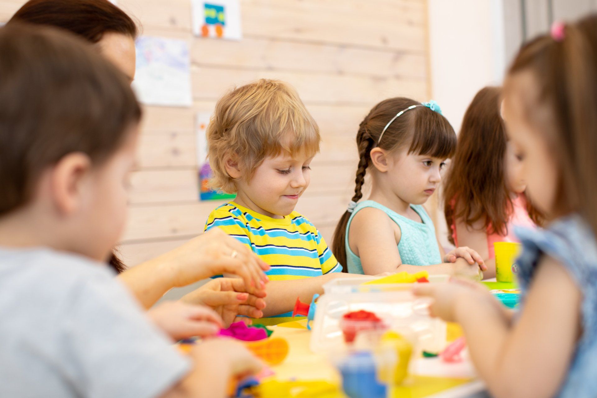 A group of children are sitting at a table playing with play dough.