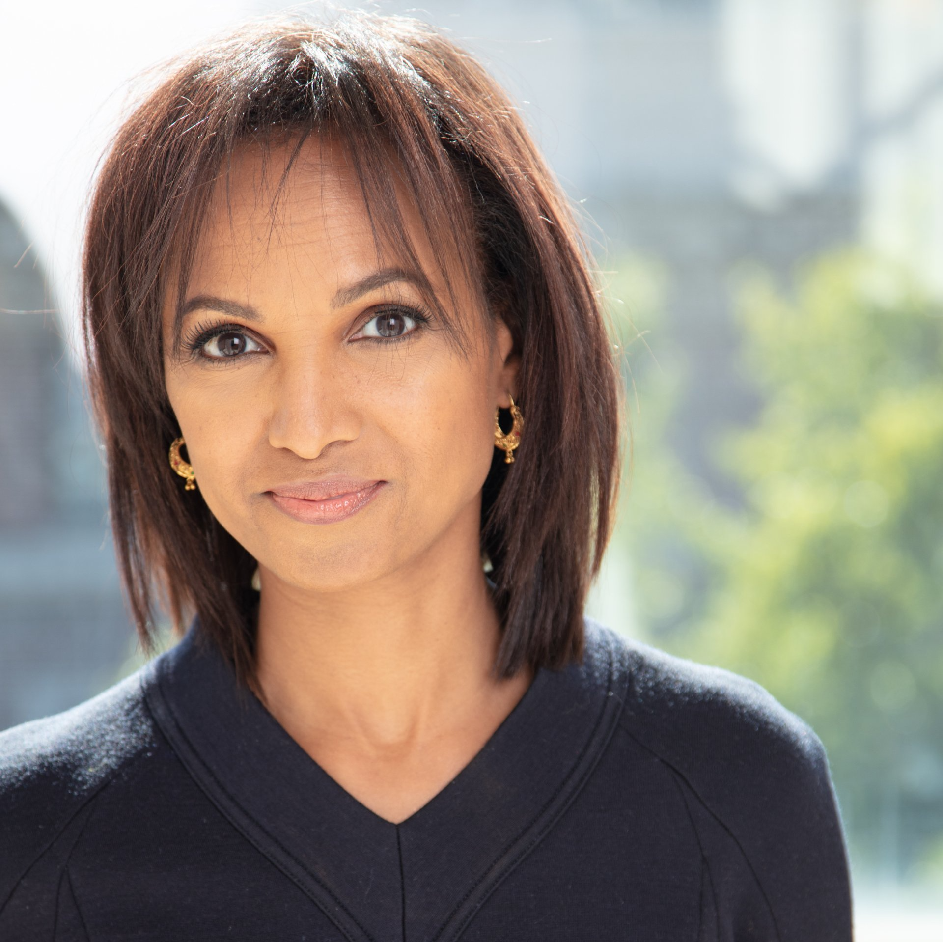 A woman wearing a black sweater and gold earrings smiles for the camera