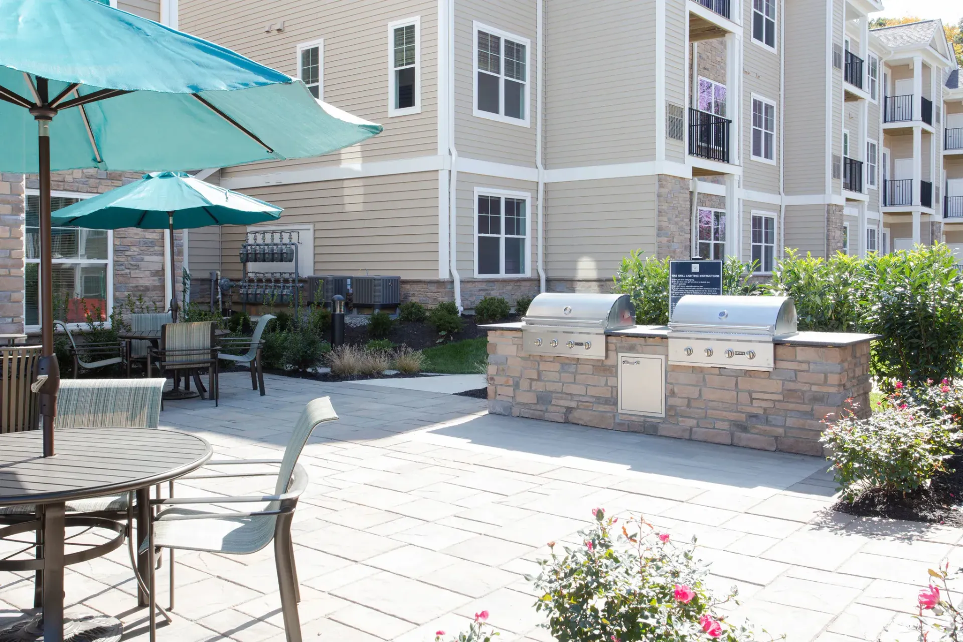 Outdoor patio with grilling stations and seating near a multi-story apartment building.