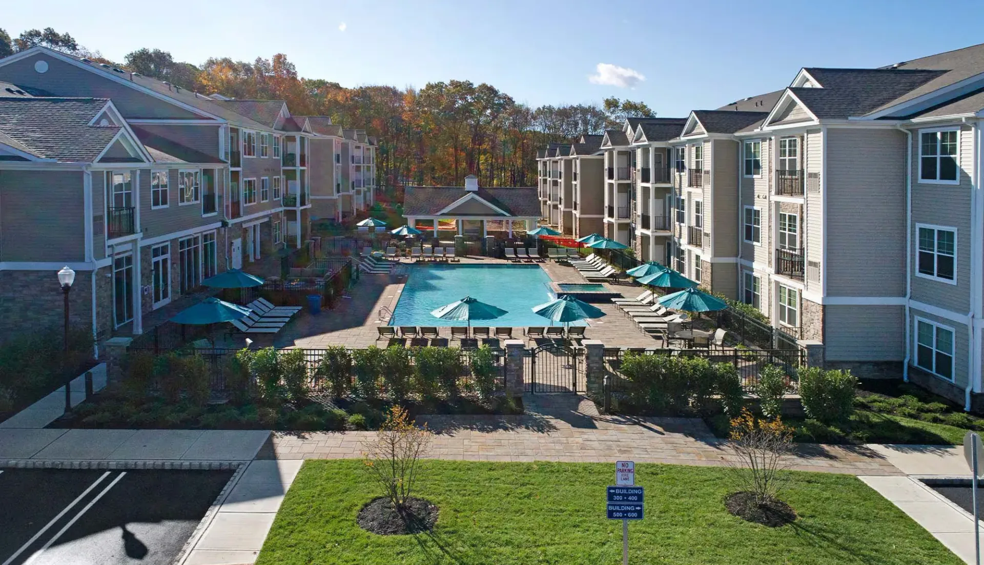 Apartment complex with pool and lounge chairs on a sunny day.