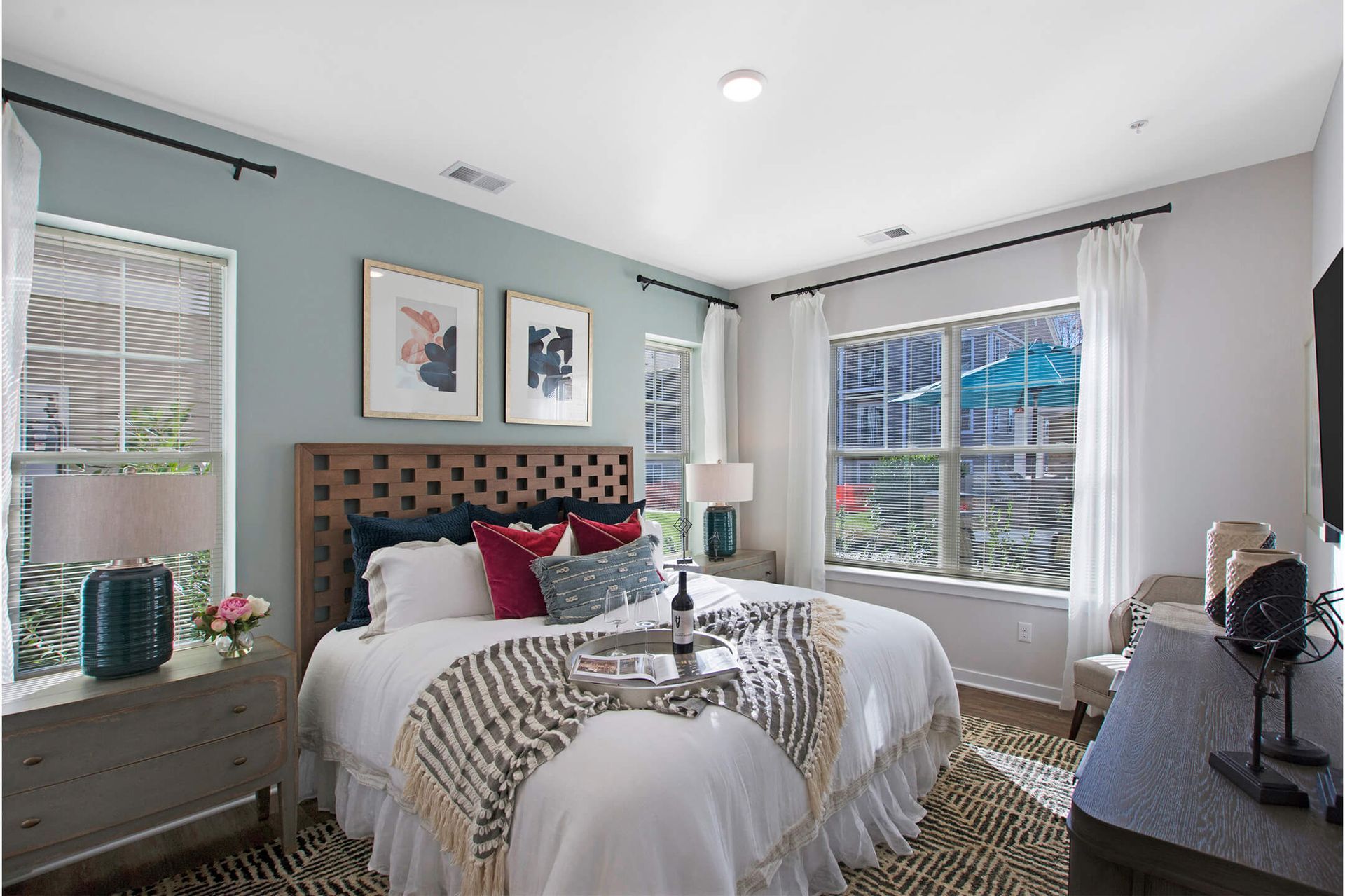 Bright apartment bedroom with a queen bed, wooden headboard, and large windows at The Parc at Roxbury in  Roxbury, NJ.