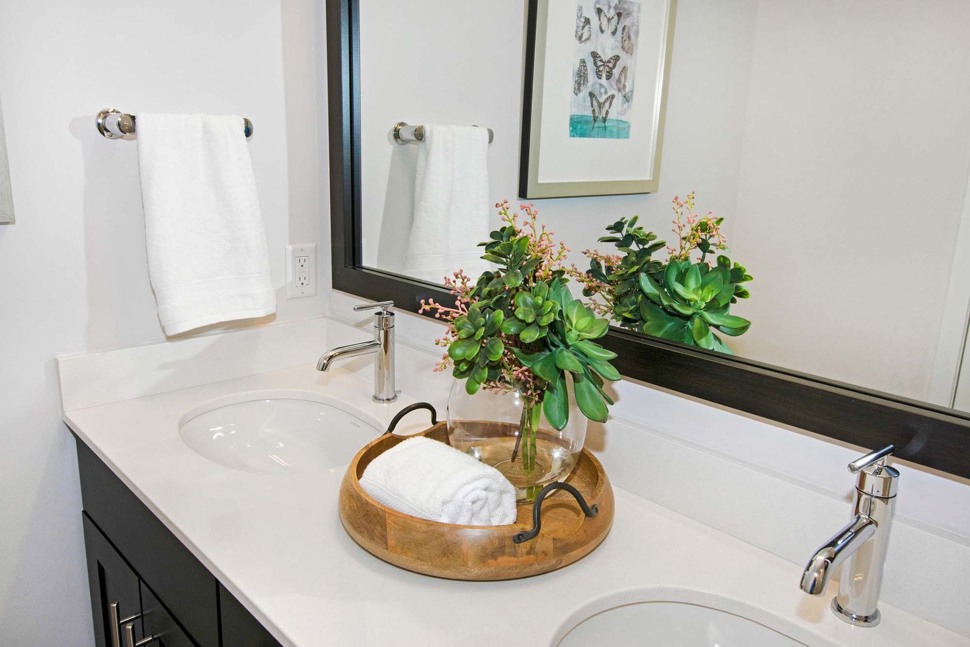 Double-sink bathroom vanity with white countertop, large mirror, towel bars, and a decorative plant at The Parc at Roxbury in  Roxbury, NJ.