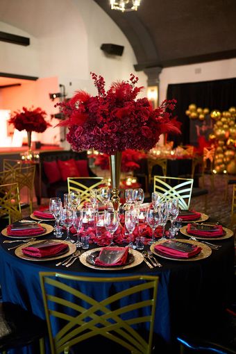 A table set for a wedding reception with red flowers in a vase.