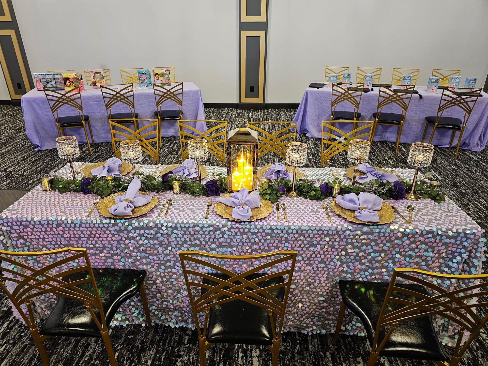 A long table with a purple tablecloth and gold chairs is set for a party.