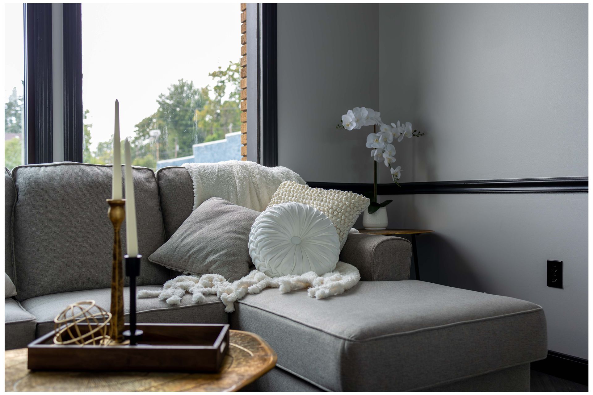 A living room with a couch , ottoman , candles and a window.