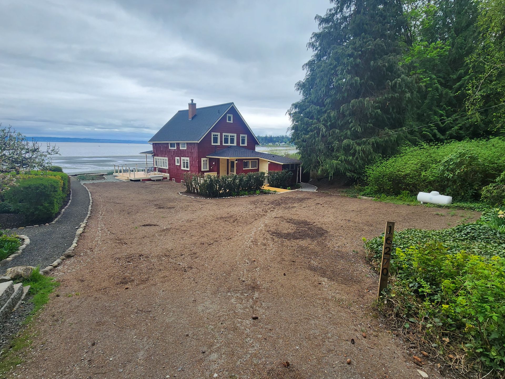 A red house is sitting on top of a dirt hill next to a body of water.