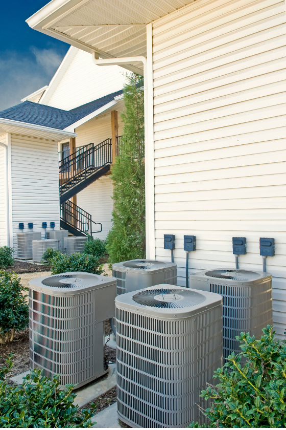 A row of air conditioners are sitting outside of a house.