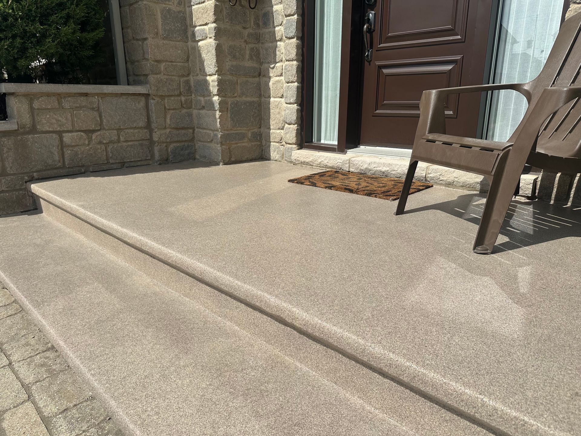 Des marches en béton beige mènent à une porte d'entrée avec une chaise sur le porche.